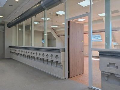 aanzicht van een van de zalen met oude stenen muur met kruizen, glazen ramen en nieuwe houten deur